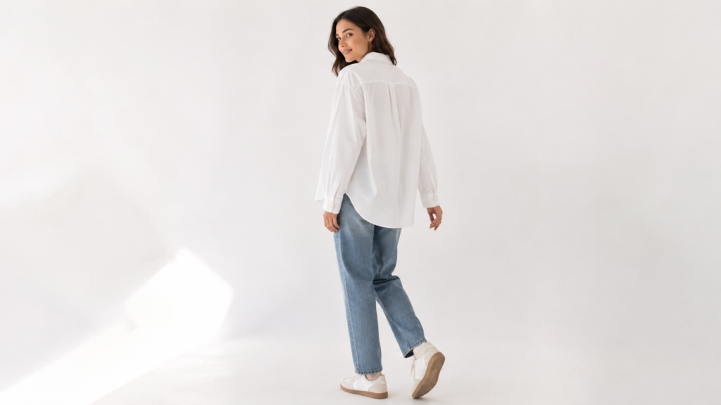 Fashion model wearing white oversized shirt and straight-leg jeans mid-movement, natural studio lighting, white seamless background, e-commerce product photography